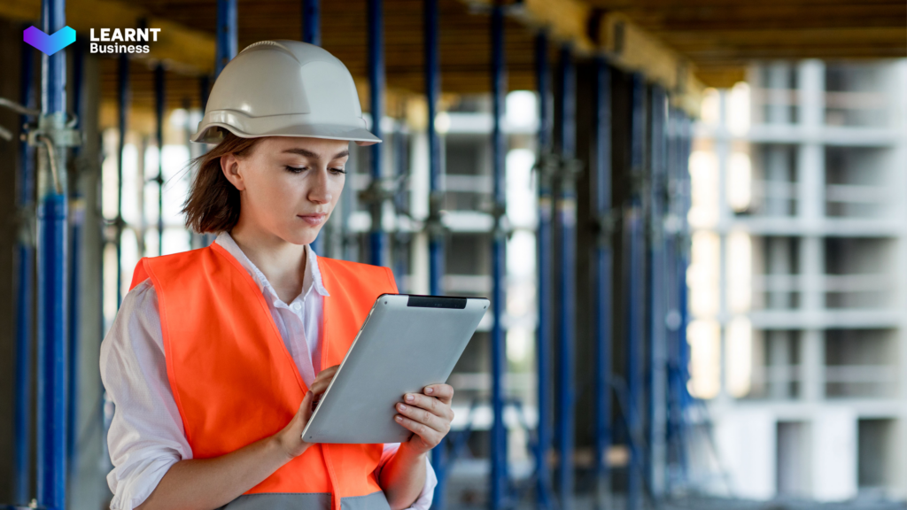 A female construction worker using a digital tablet on-site for training and compliance tracking, wearing safety gear and a hard hat.