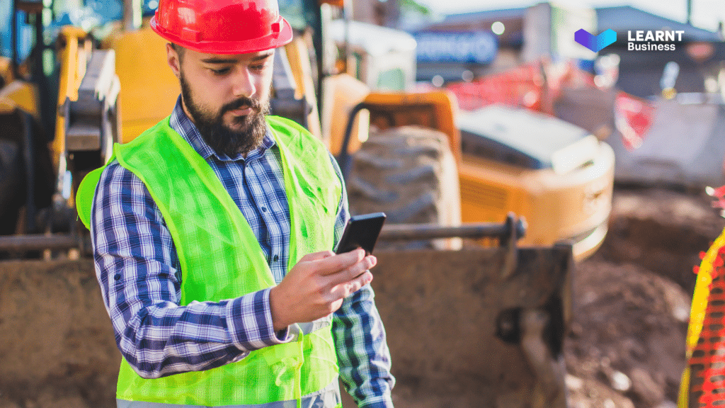 A construction worker in safety gear using a mobile device on-site.