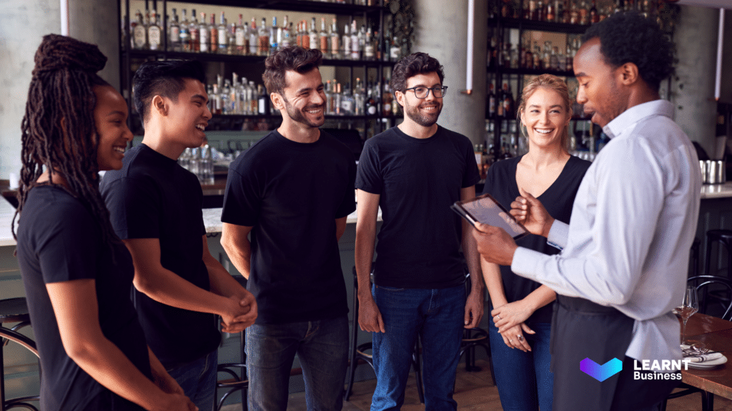 Hospitality staff receiving digital training from a manager using a tablet at a modern bar, ensuring seamless onboarding and skill development.