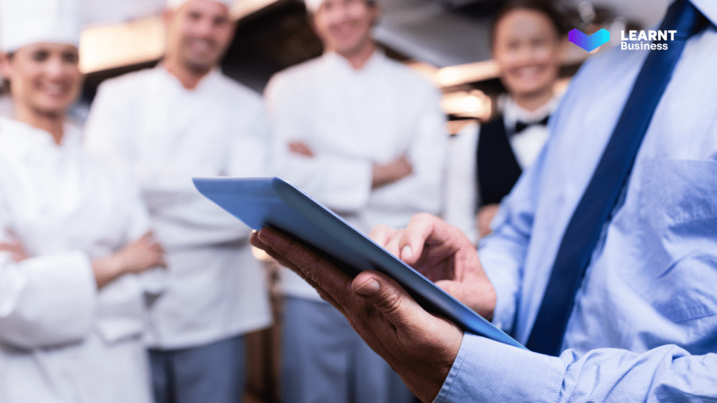 Restaurant kitchen staff attentively listening to a digital training session conducted by a manager using a tablet, enhancing food safety and compliance.