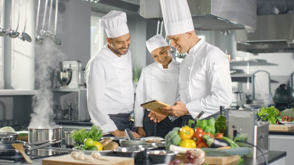 Kitchen staff reviewing digital training on a tablet in a professional restaurant kitchen