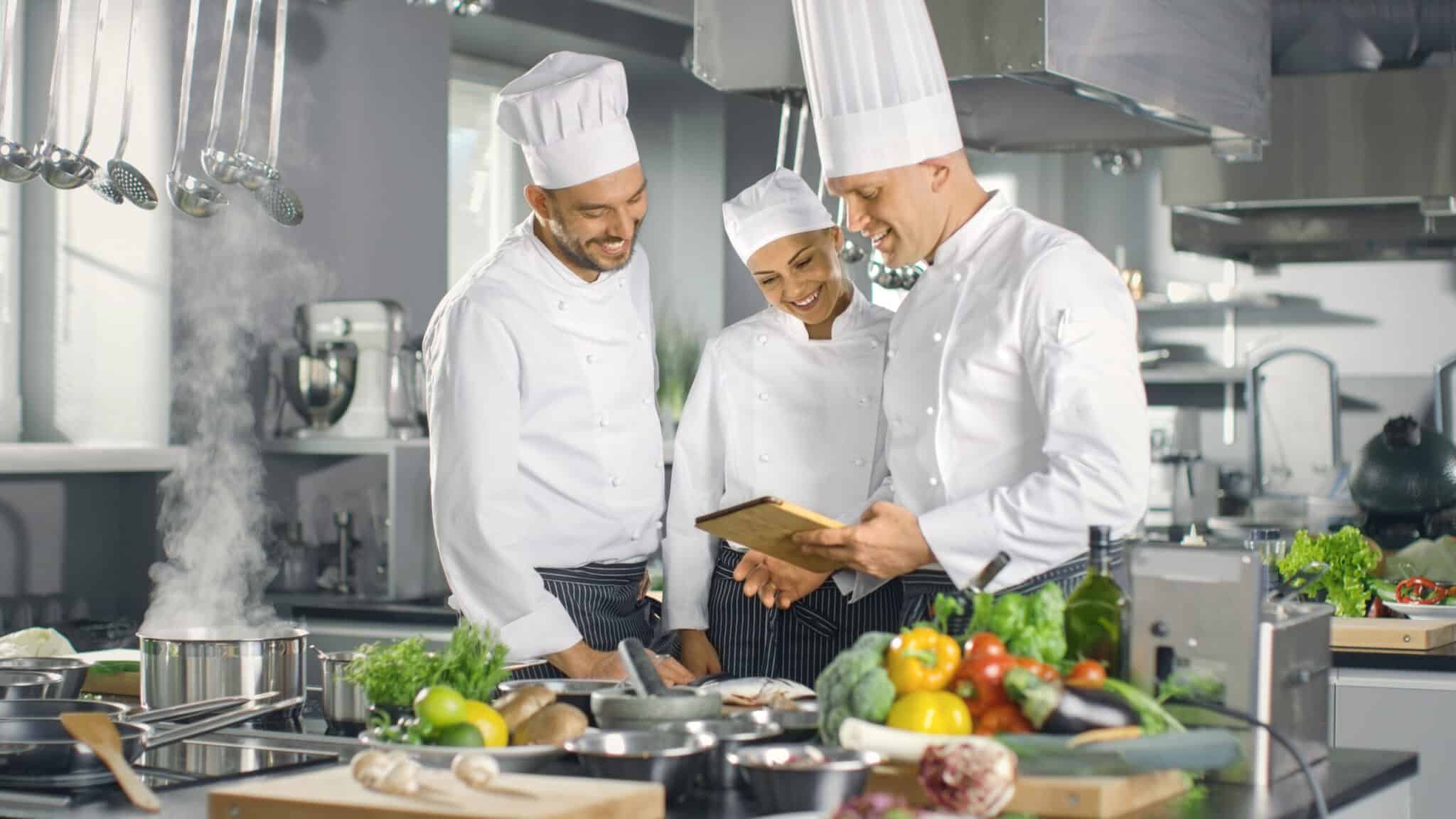 Kitchen staff reviewing digital training on a tablet in a professional restaurant kitchen