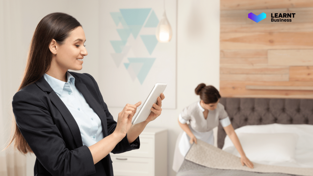 Hospitality manager using a tablet to oversee hotel staff training while a housekeeper prepares a room, ensuring efficiency and quality service delivery.